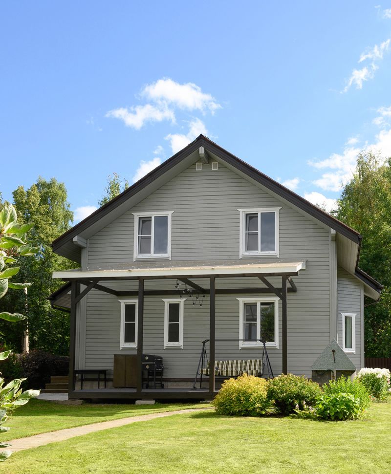Gray two-story house with a porch, green lawn, and blue sky
