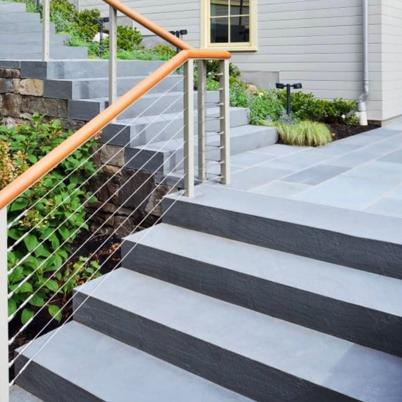 Concrete steps with cable railing and wooden handrail leading up to a light gray home