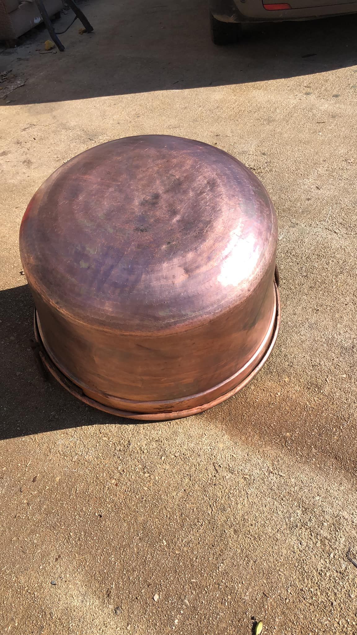 Una grande tinozza o pentola rotonda di rame è appoggiata capovolta su una superficie di cemento.