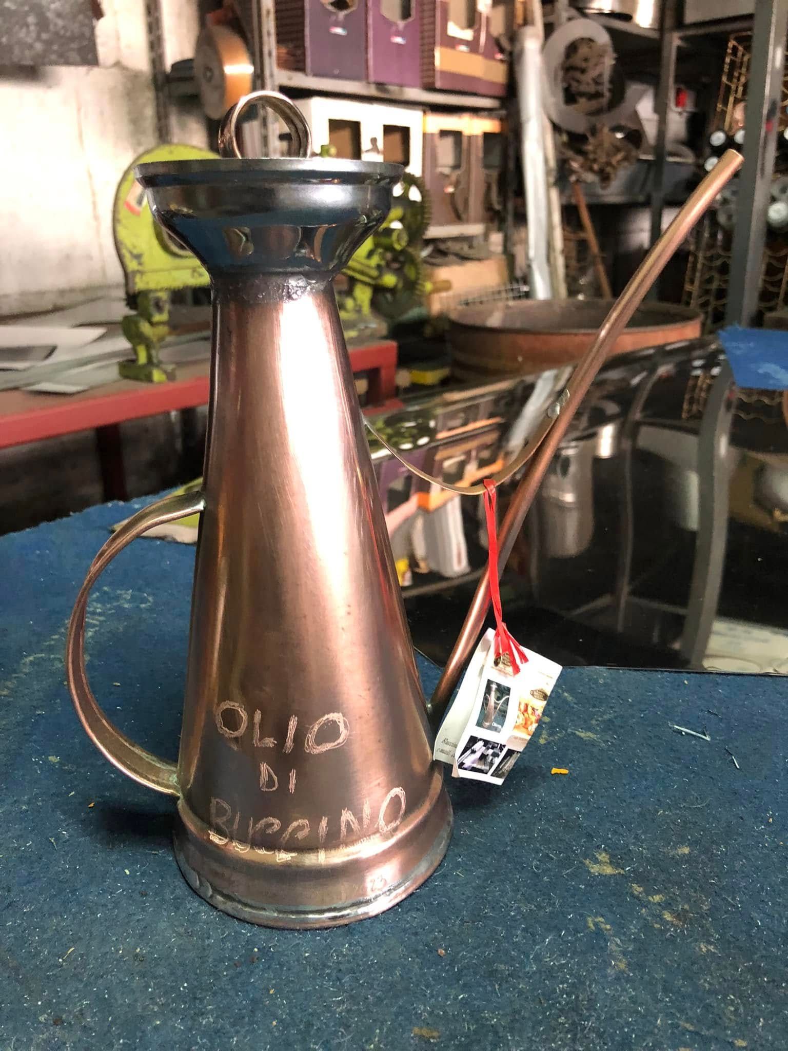 Un versatore per olio in metallo color rame con incisa la scritta 