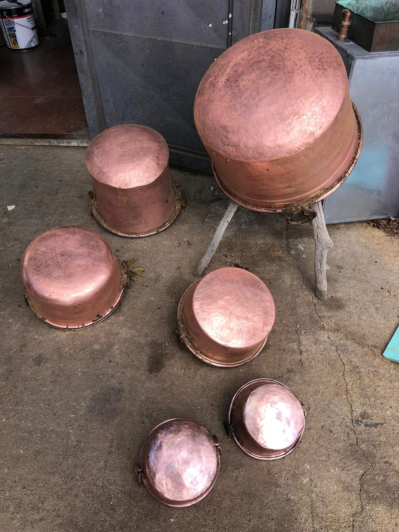 Cinque pentole di rame di diverse dimensioni, capovolte su una superficie di cemento.