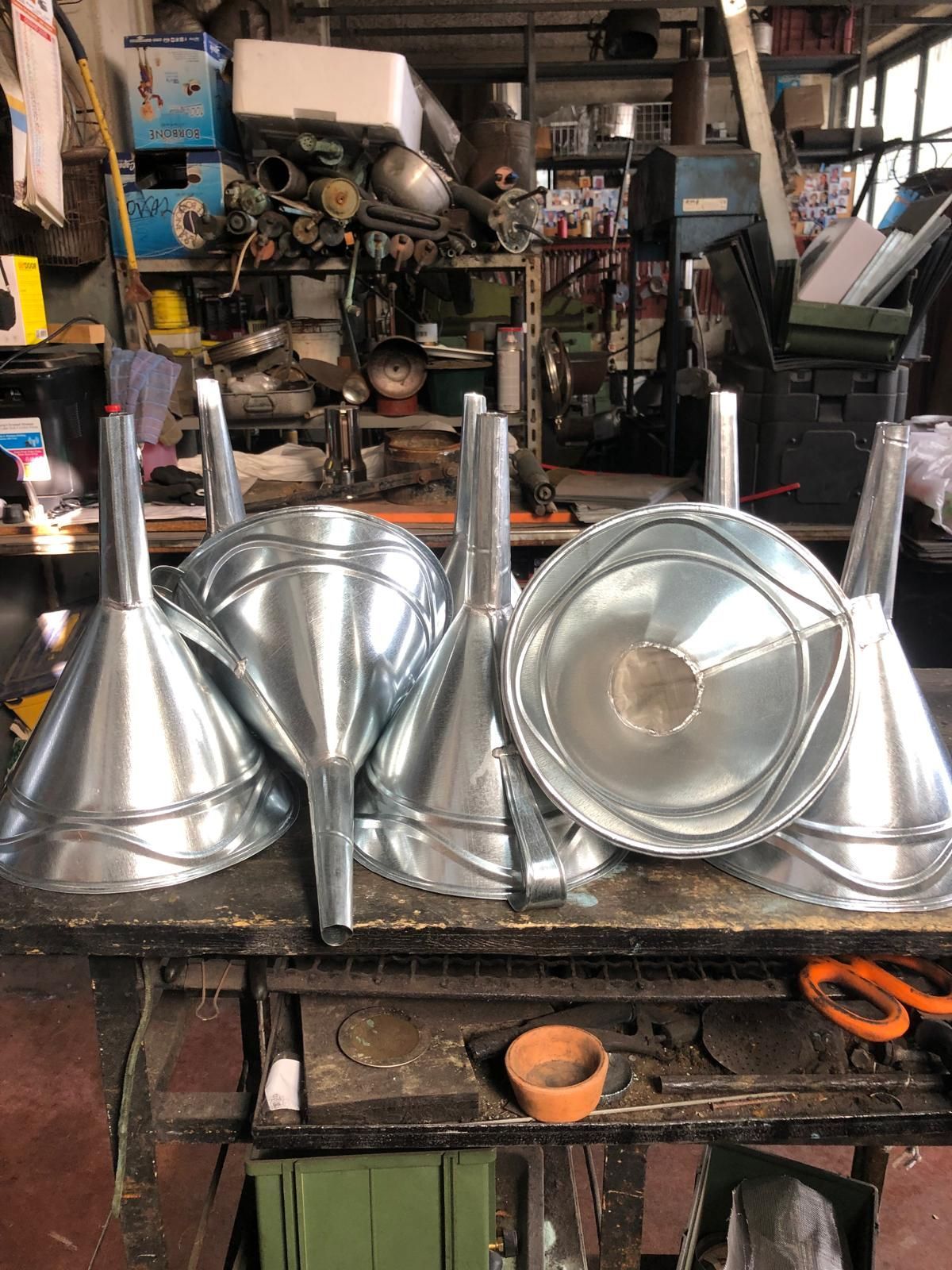 Diversi imbuti conici metallici disposti su un banco da lavoro in legno ingombro di oggetti in un'officina.