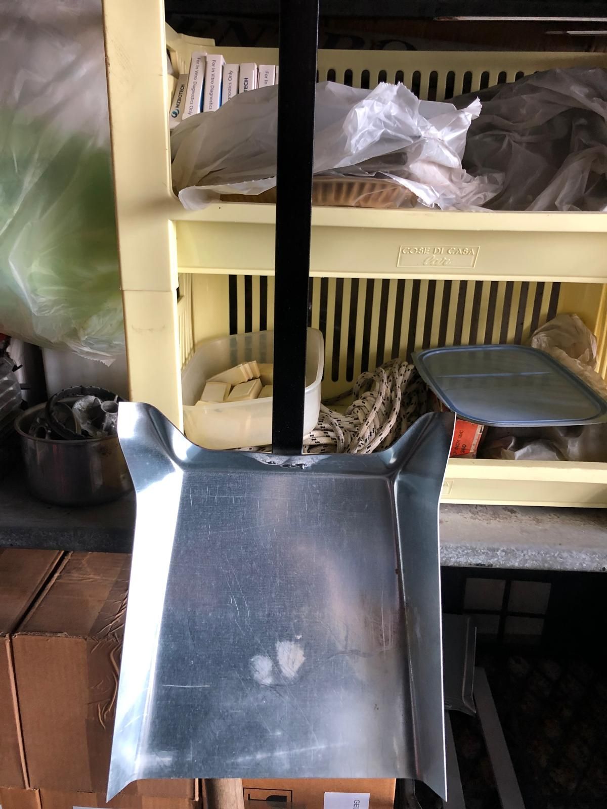 Una paletta di metallo con manico nero, posizionata davanti a un contenitore di plastica giallo.