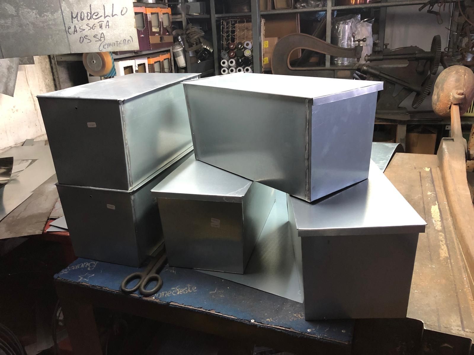 In un'officina, diversi contenitori metallici rettangolari sono appoggiati su un banco da lavoro.
