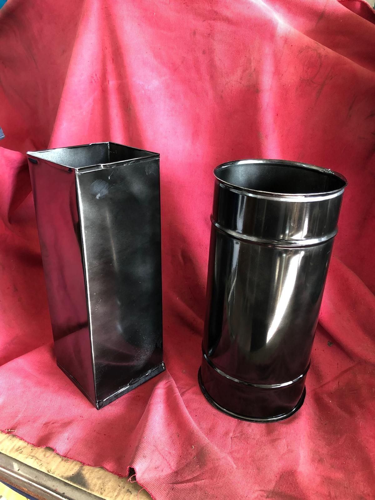 Due contenitori neri lucidi, uno rettangolare e uno cilindrico, poggiati su uno sfondo di tessuto rosso drappeggiato.