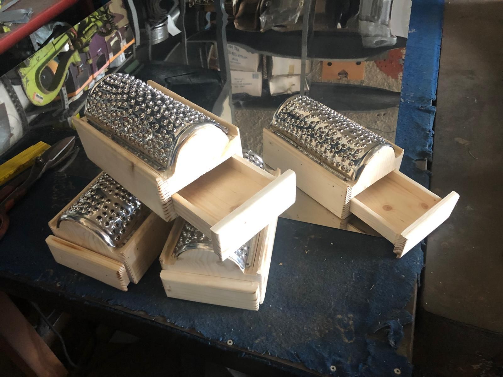 Quattro scatole di legno fatte a mano, ciascuna sormontata da una grattugia metallica capovolta, appoggiate su una superficie scura in un'officina.