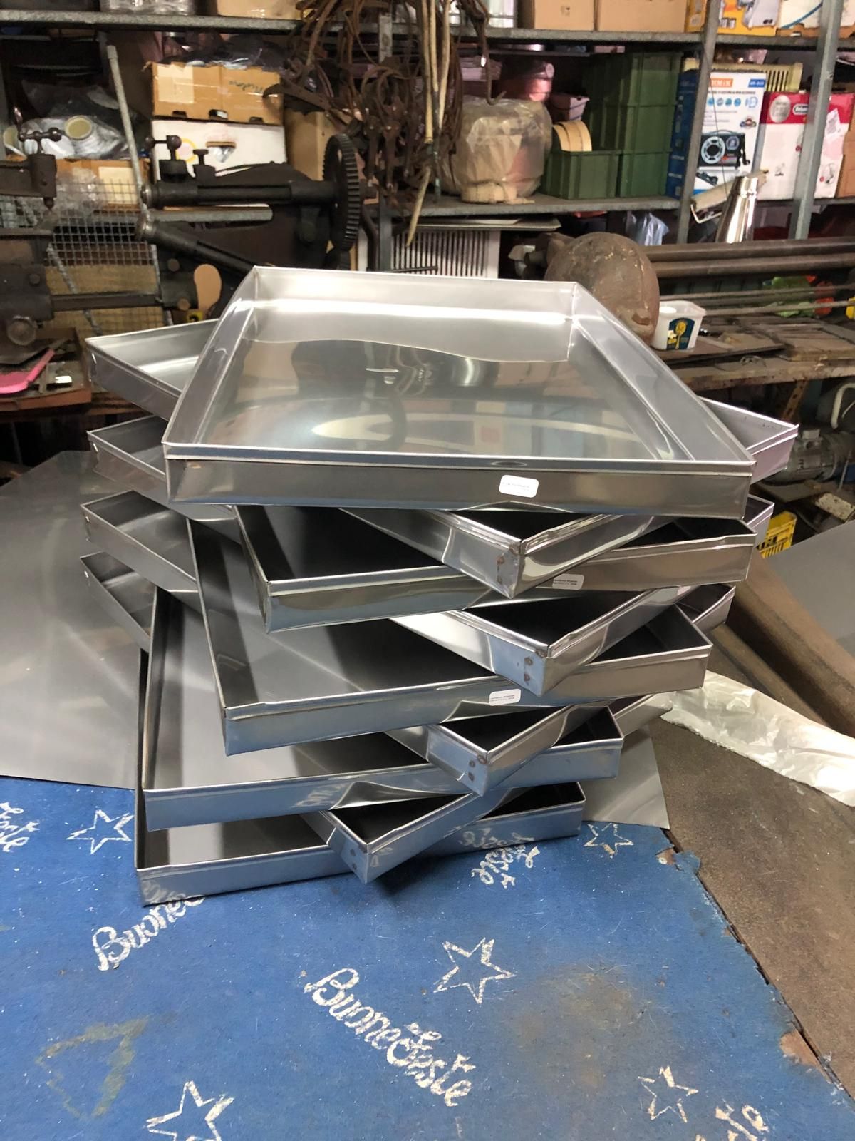In un'officina, una pila di diversi vassoi metallici rettangolari è appoggiata su una superficie blu.