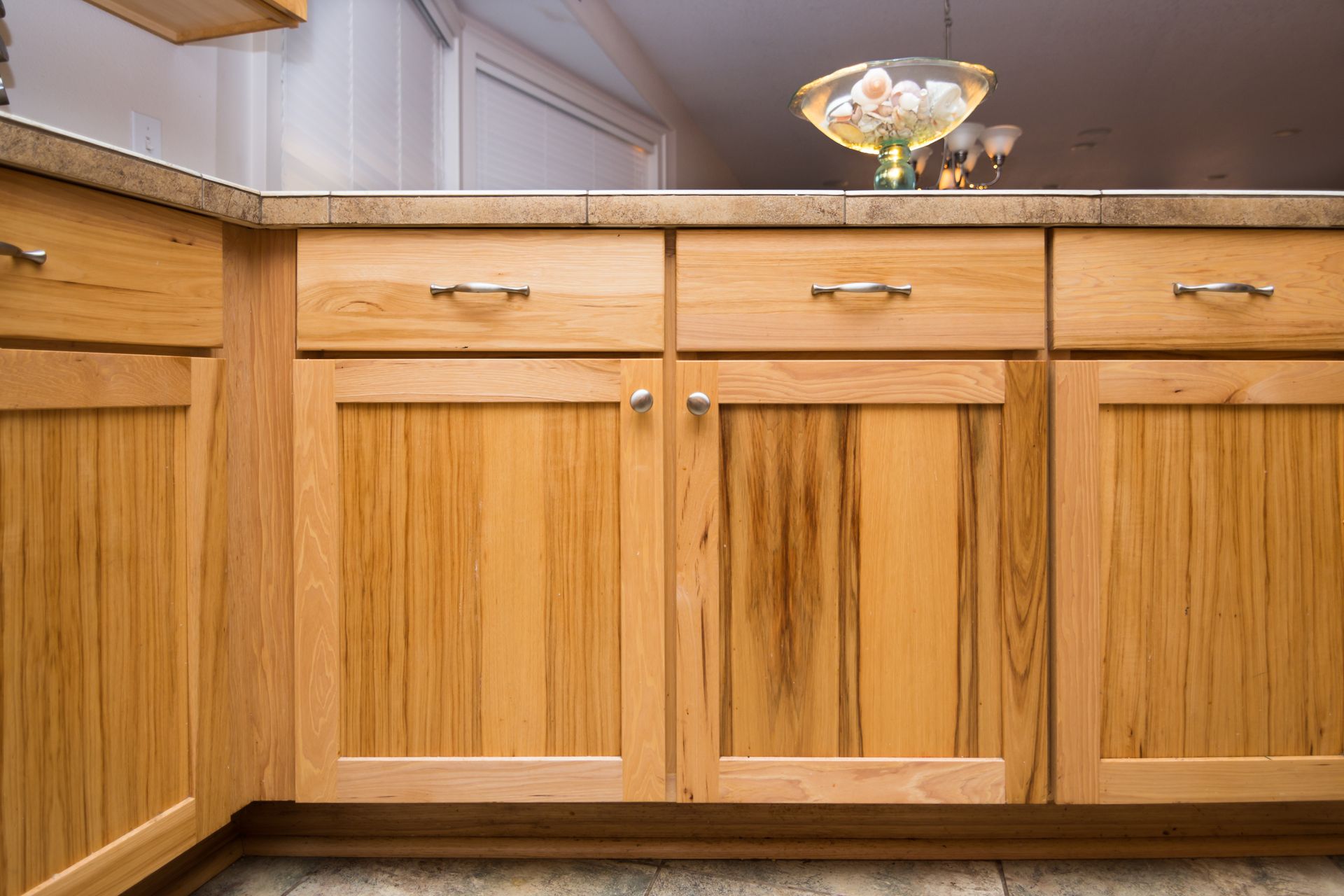 A kitchen with wooden cabinets and drawers and a bowl of seashells on the counter.