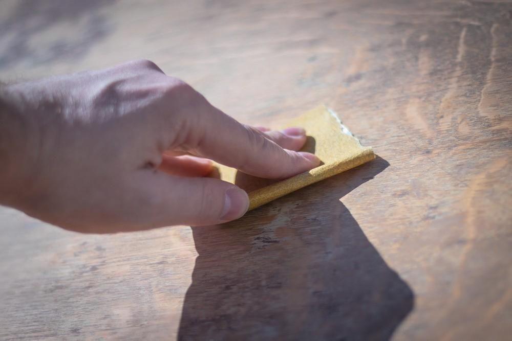 A person is sanding a piece of wood with a sandpaper.