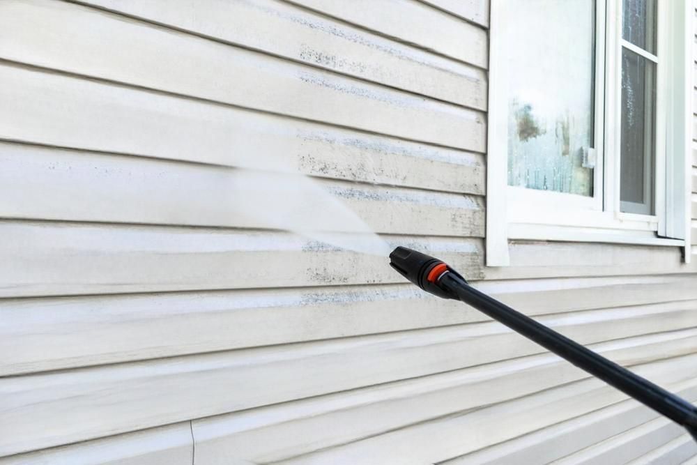 A person is cleaning the side of a house with a high pressure washer.