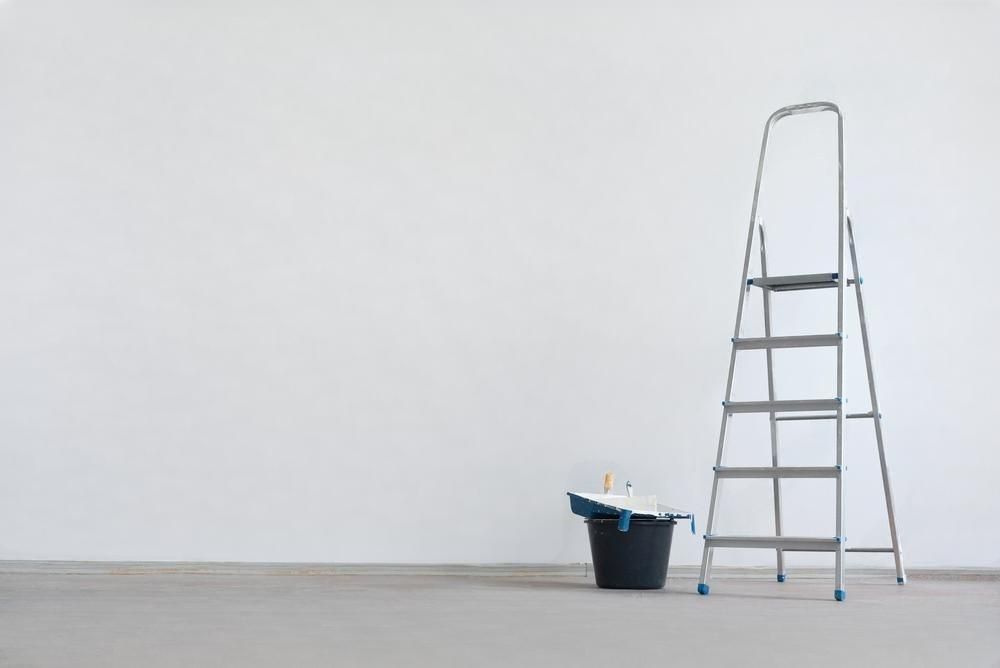 A ladder and bucket are sitting in front of a white wall.