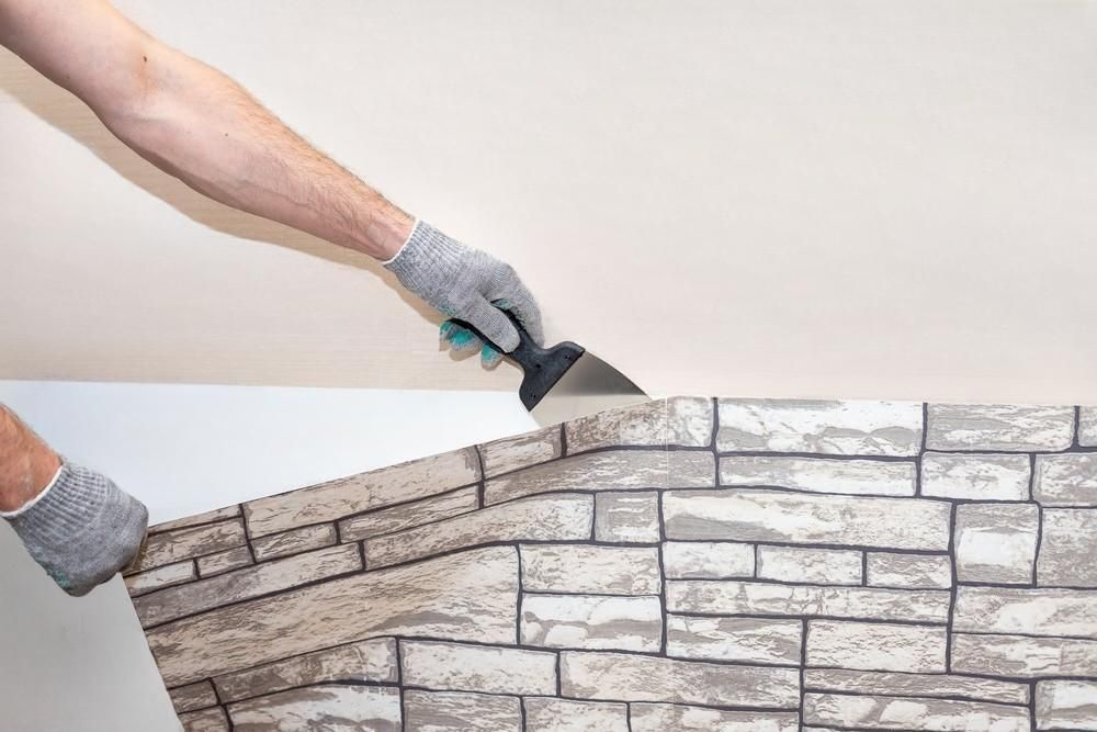 A person is applying wallpaper to a wall with a spatula.