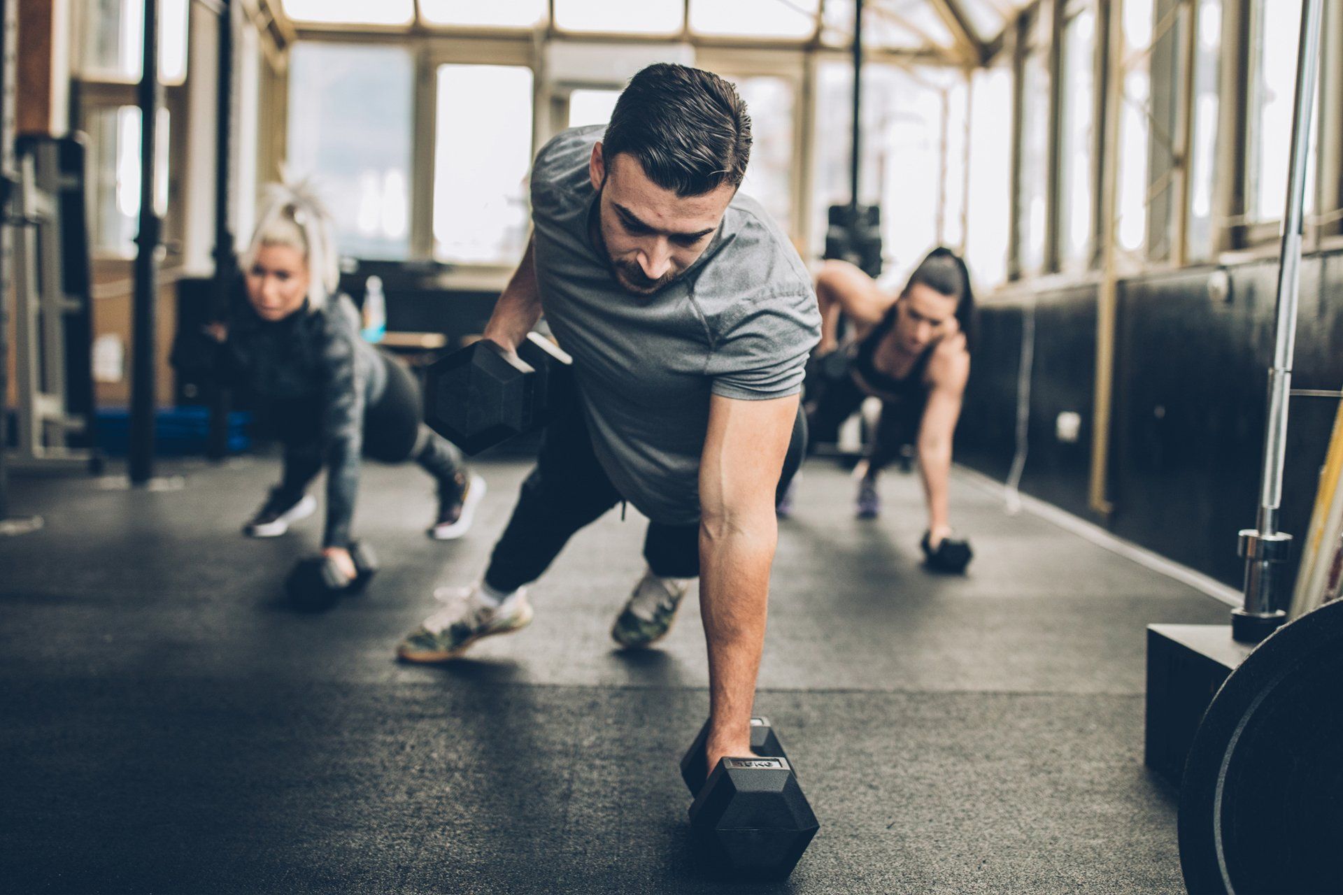 a group of people are doing push ups with dumbbells in a gym .