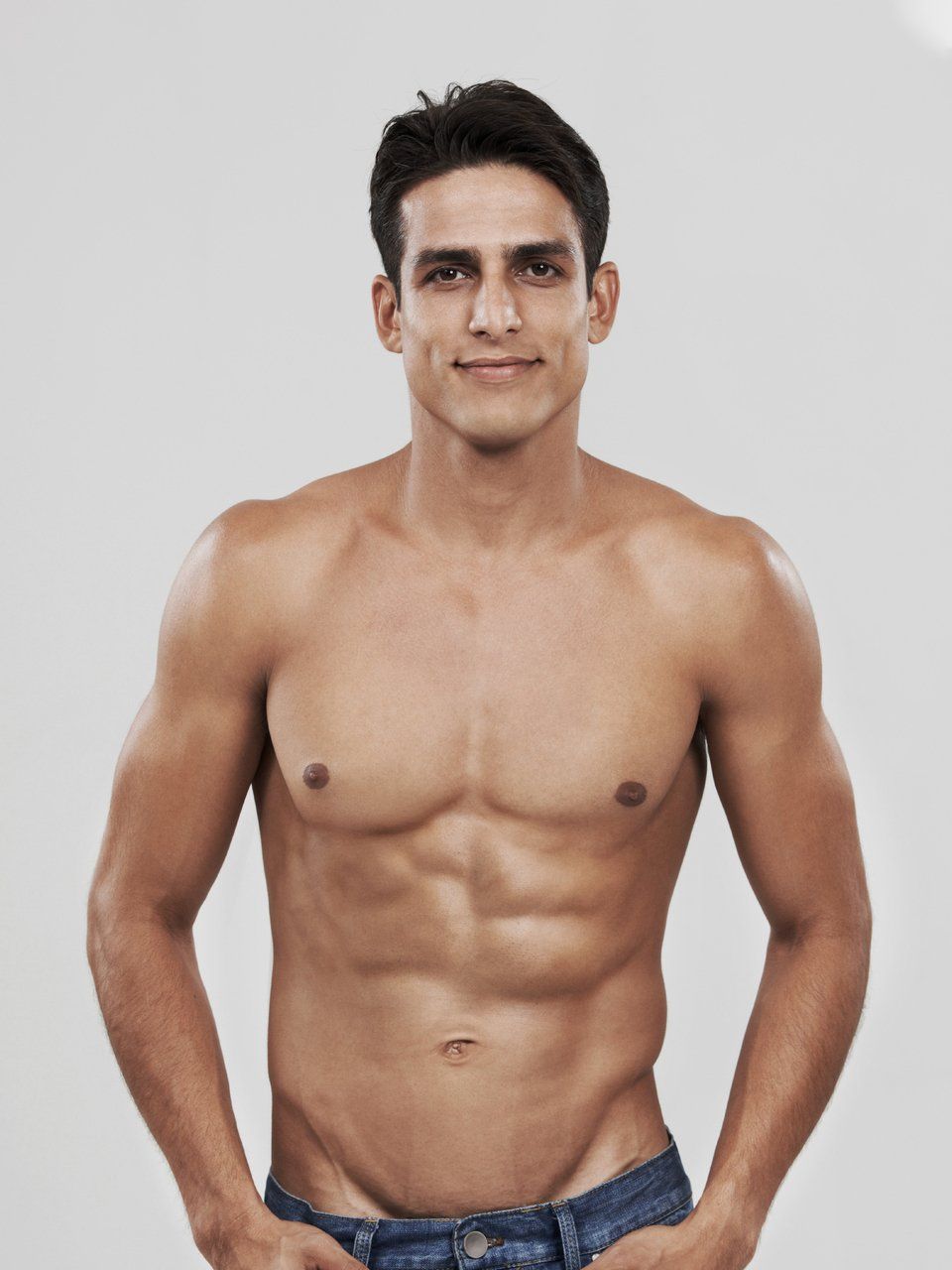 a shirtless man is standing with his hands in his pockets .