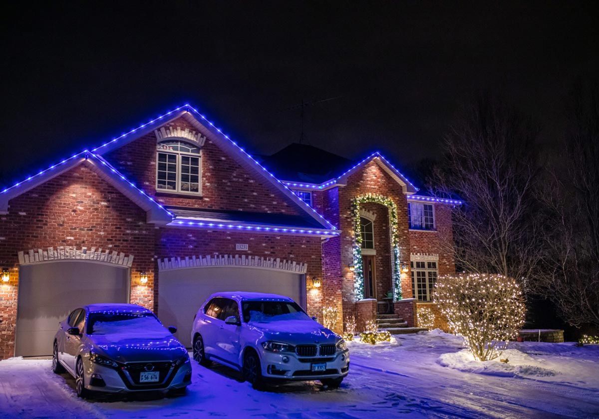 Two cars are parked in front of a house decorated with christmas lights.