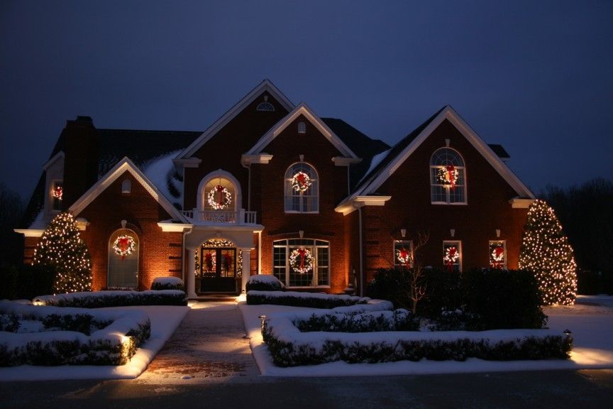 A large red brick house is decorated with christmas lights and wreaths