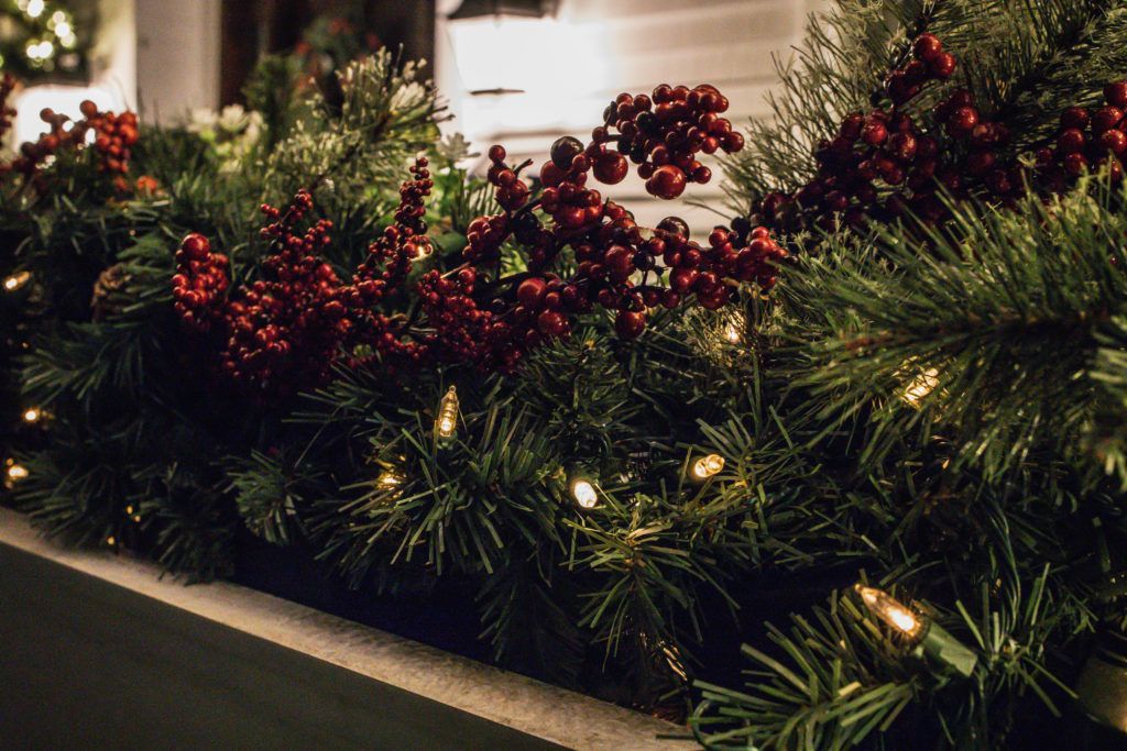 A christmas garland with red berries and lights is sitting in front of a house.
