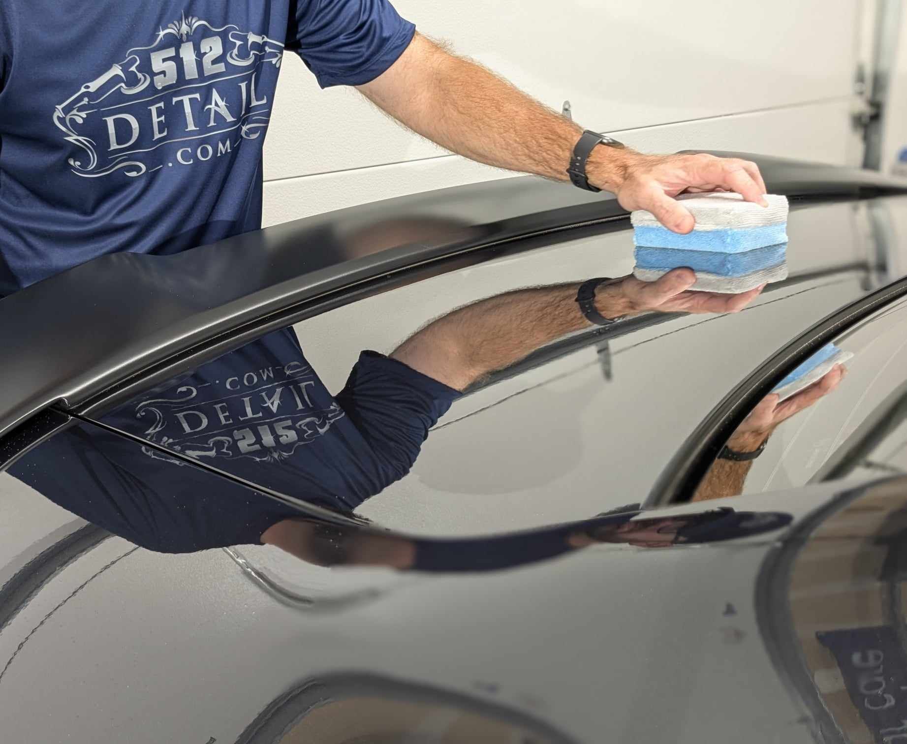 A person wearing black gloves is applying coating to red car.