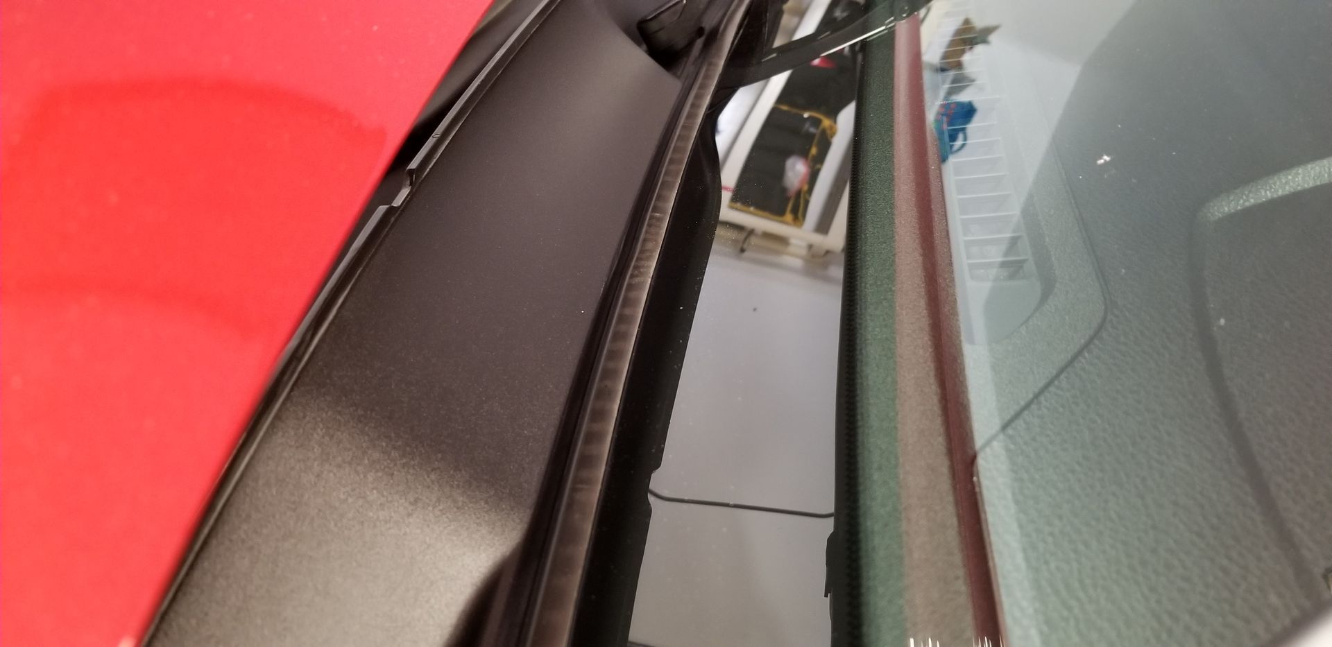 A close up of a car windshield with a red car in the background.