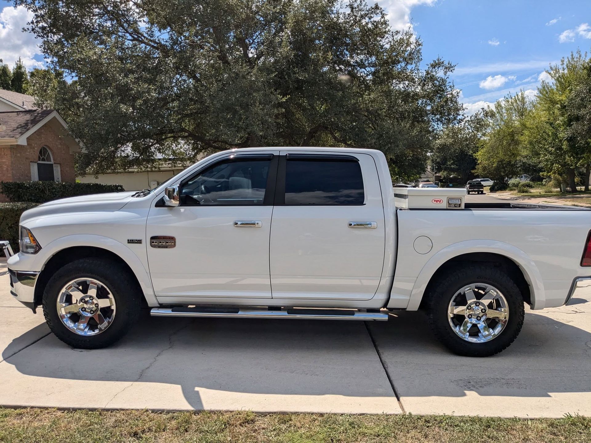 White Dodge Ram pickup truck parked in a driveway, chrome wheels, clear day.
