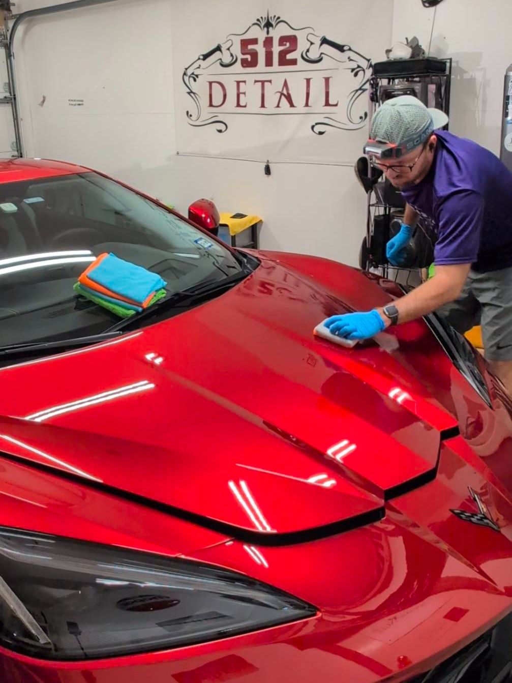 A man is polishing the hood of a red sports car