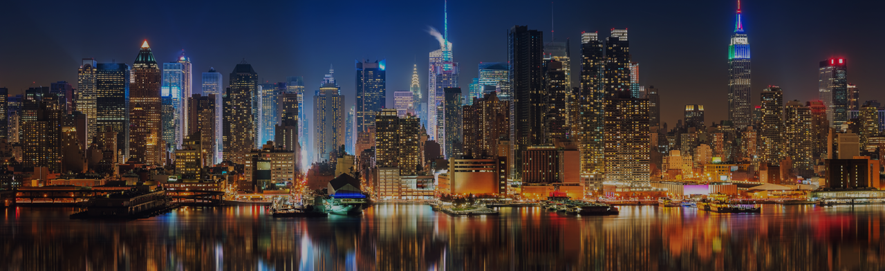 A blurry picture of the New York skyline at night with the East River river in the foreground.