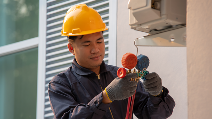 A man wearing a hard hat and gloves is working on an air conditioner.