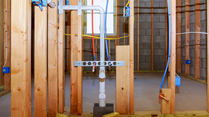 A room in a house under construction with pipes and wires.