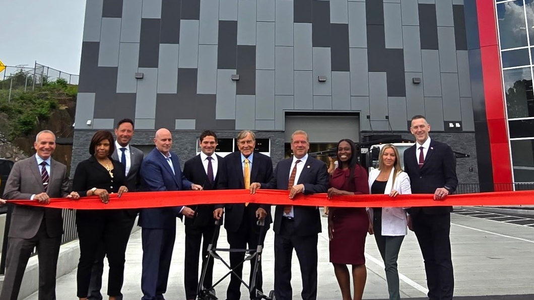 Group of people cutting a red ribbon in front of a gray building with a red vertical accent