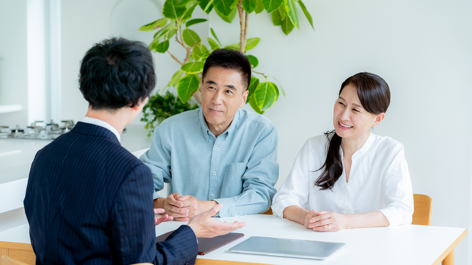 A buyer's agent with an older couple at a table in a bright room.