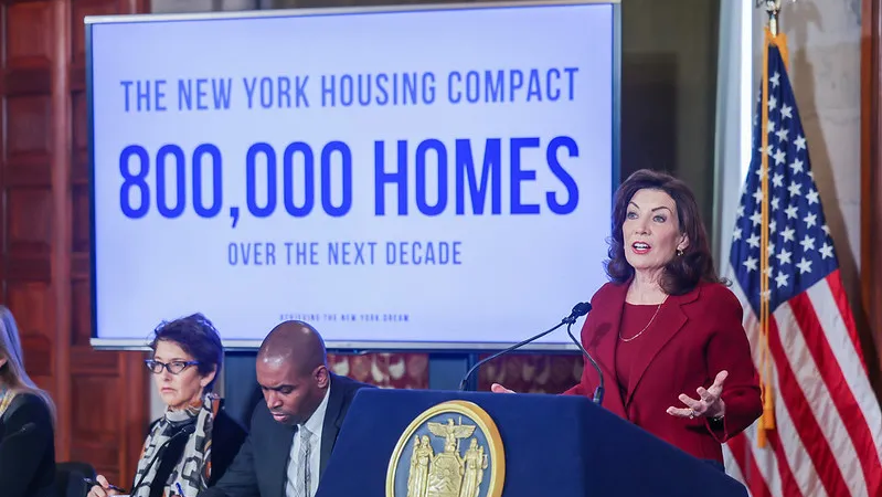 Kathy Hochul, Governor of New York,  is standing at a podium in front of a sign that says 800,000 homes over the next decade.