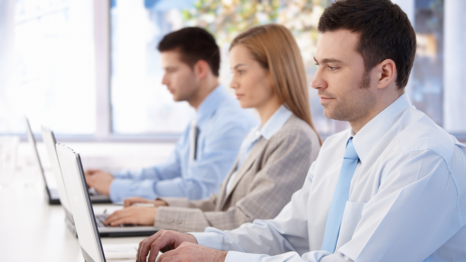 A group of people are sitting in a row using laptops.