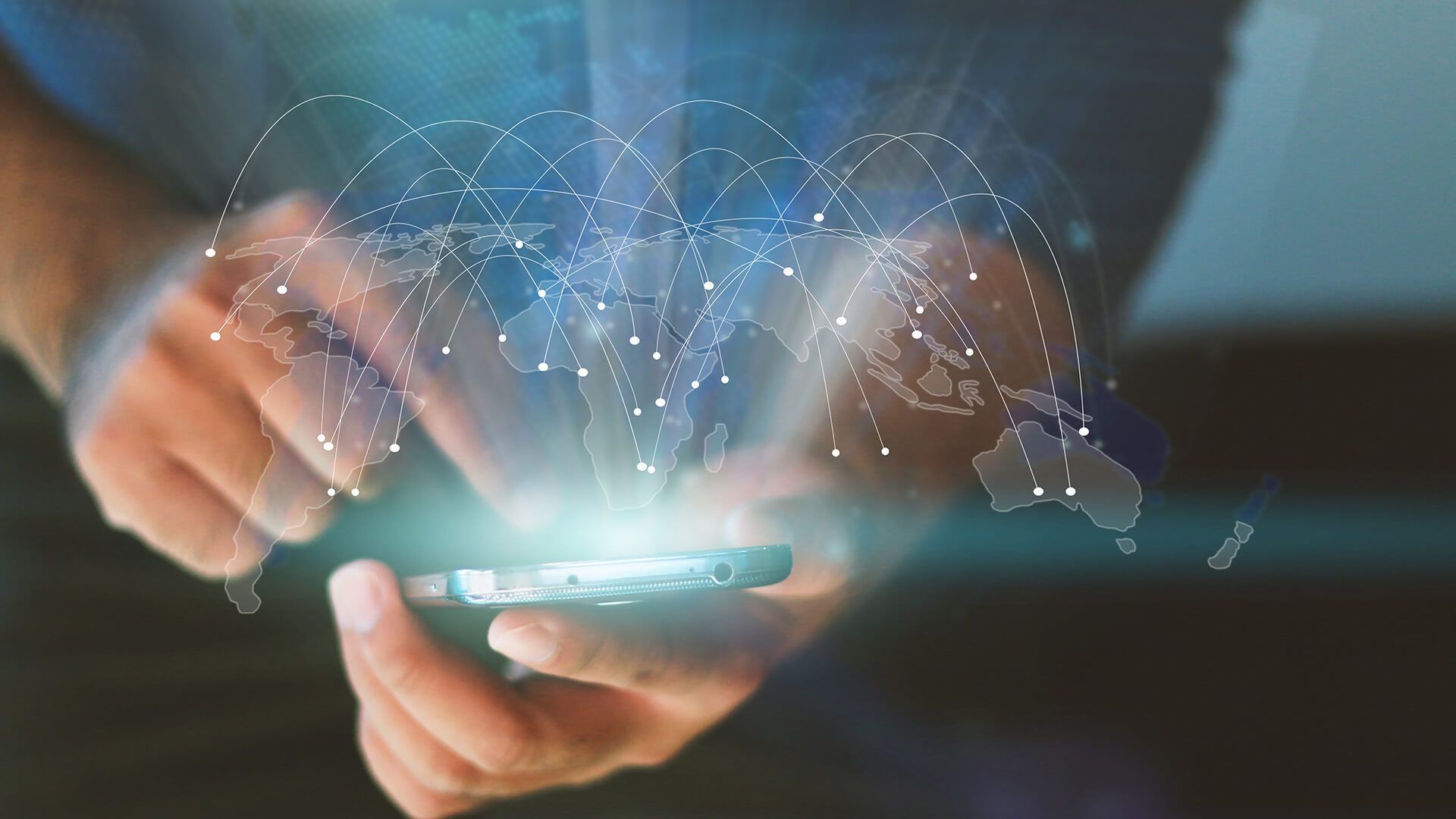 A person is holding a cell phone in their hands with a map of the world coming out of it.