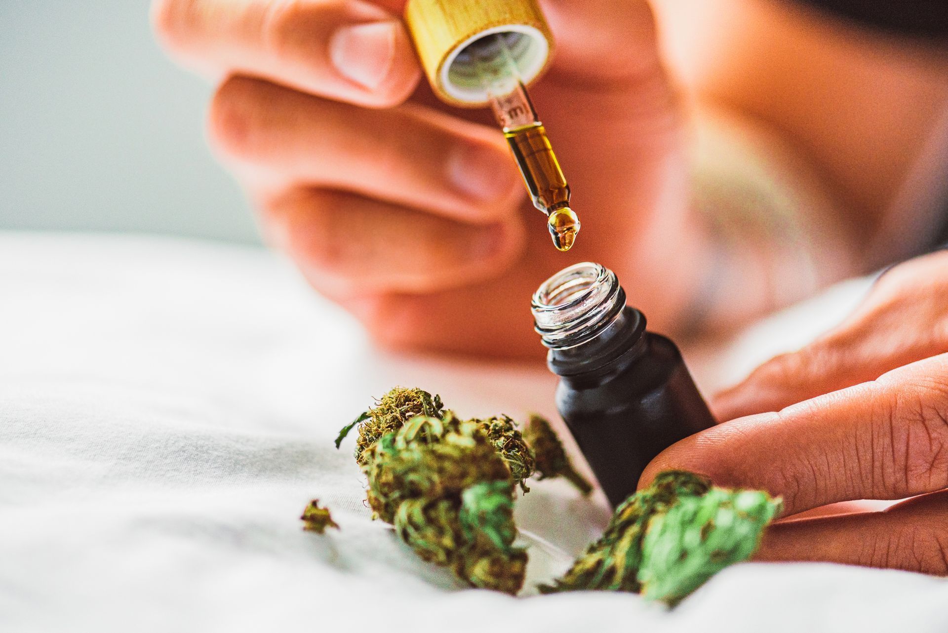 Close-up of a person using a dropper to extract CBD oil from a bottle, with dried cannabis buds in the foreground.