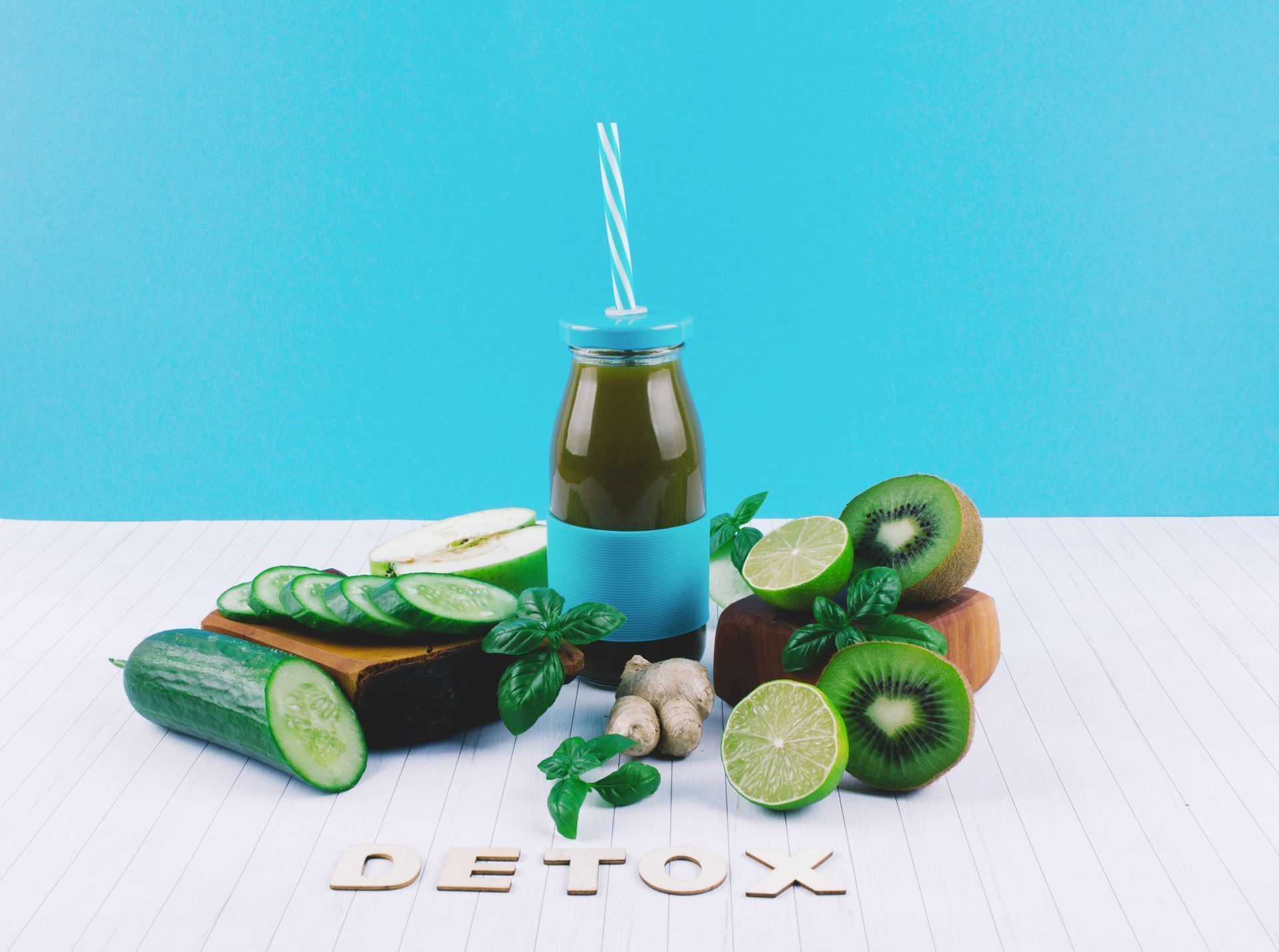 A bottle of green juice with a straw surrounded by fruits and vegetables on a table.