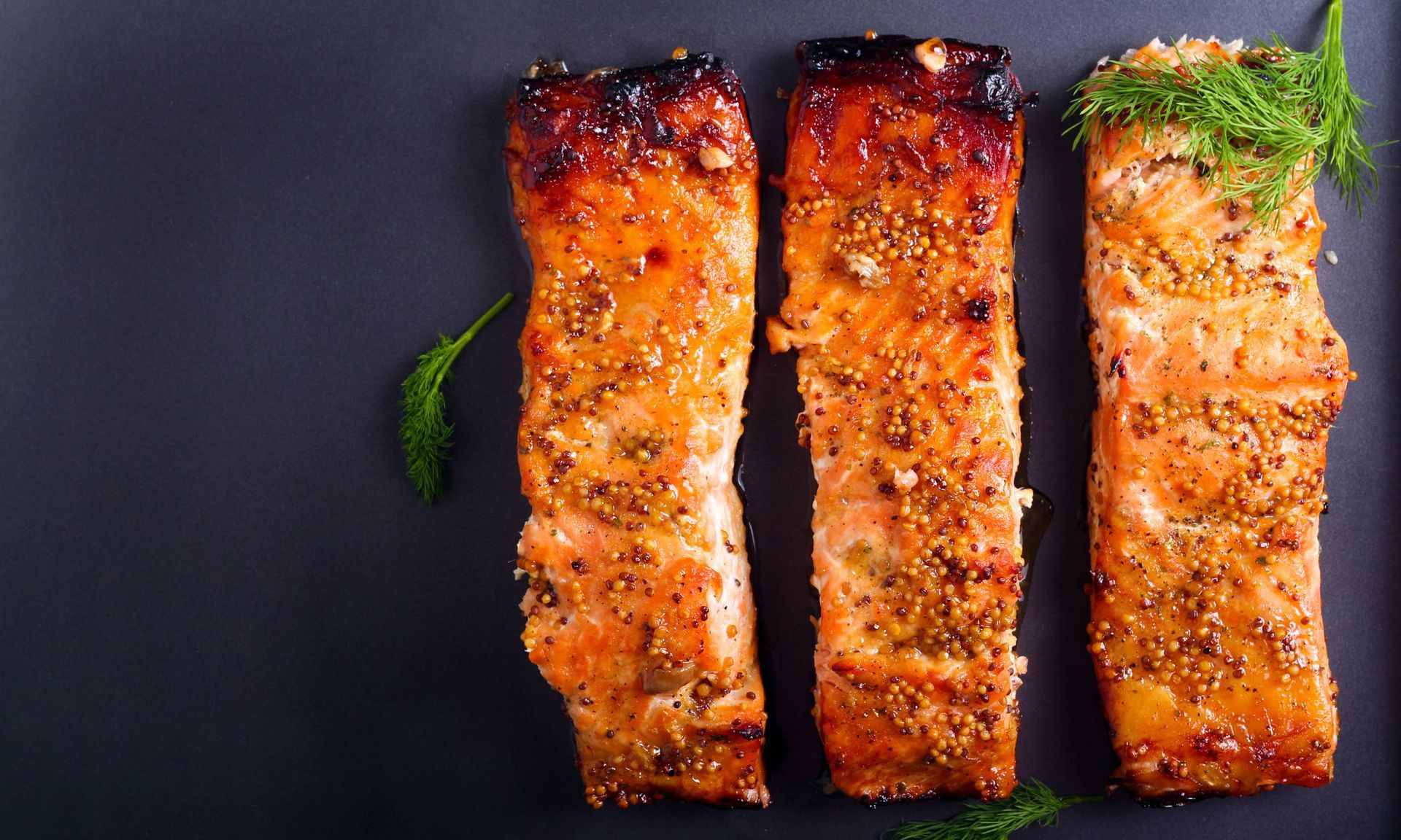 Three pieces of grilled salmon are on a black plate.