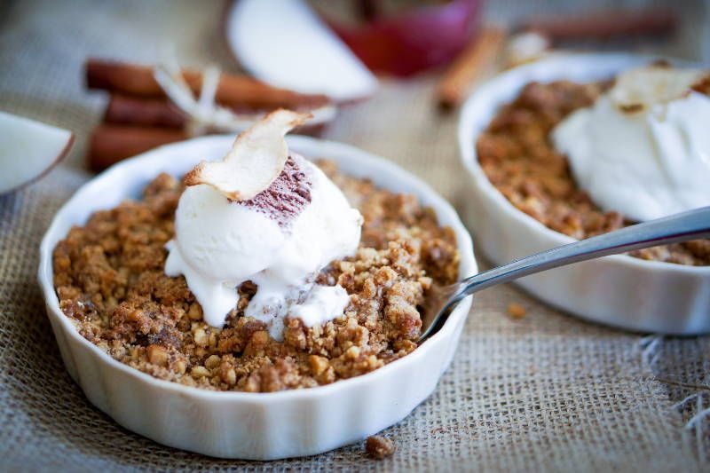 A bowl of apple crisp with ice cream and a spoon in it.