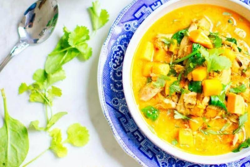 There is a bowl of soup on a plate with a spoon.