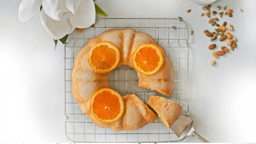 A bundt cake with oranges on it is sitting on a cooling rack.