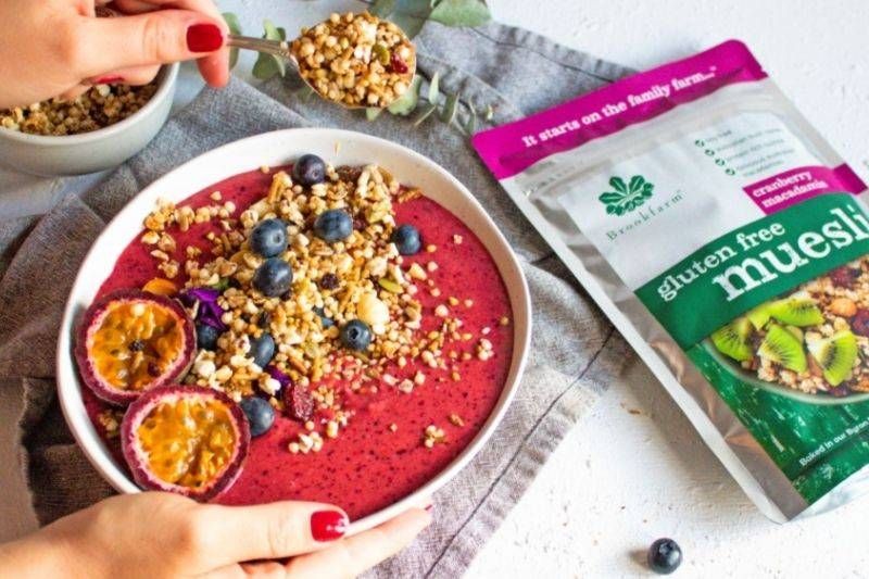 A person is holding a bowl of food next to a bag of gluten free muesli.