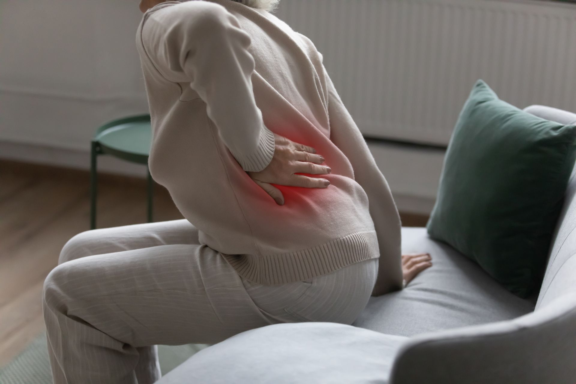 Person sitting, hand on lower back highlighted in red, indicating pain.