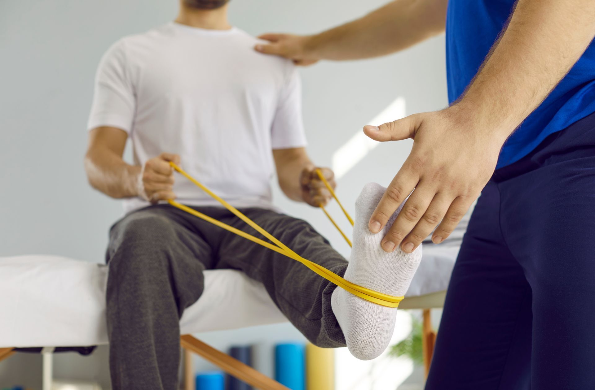 Man doing physical therapy with assistance, using a resistance band in a clinic.