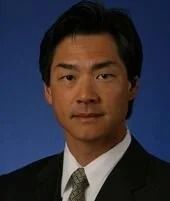 Man in suit, looking forward, against a blue background.