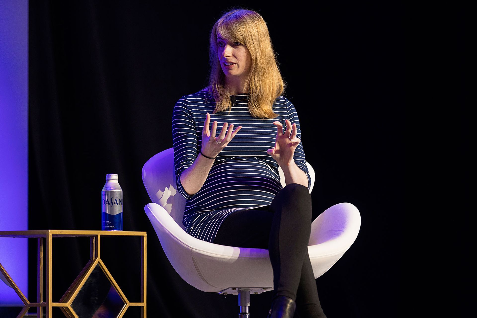 A woman is sitting in a white chair on a stage.