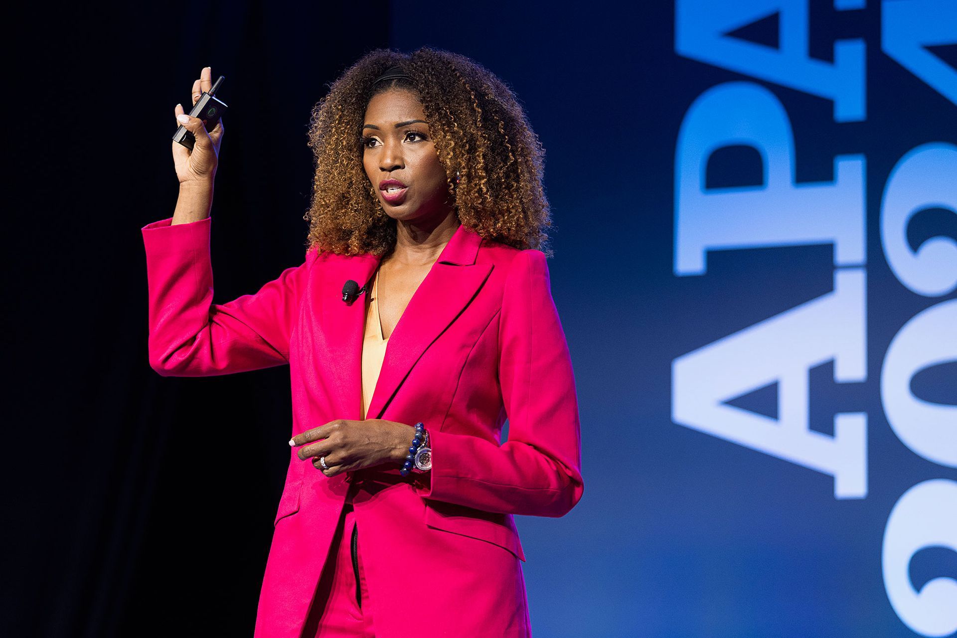 A woman in a pink suit is giving a speech on a stage.