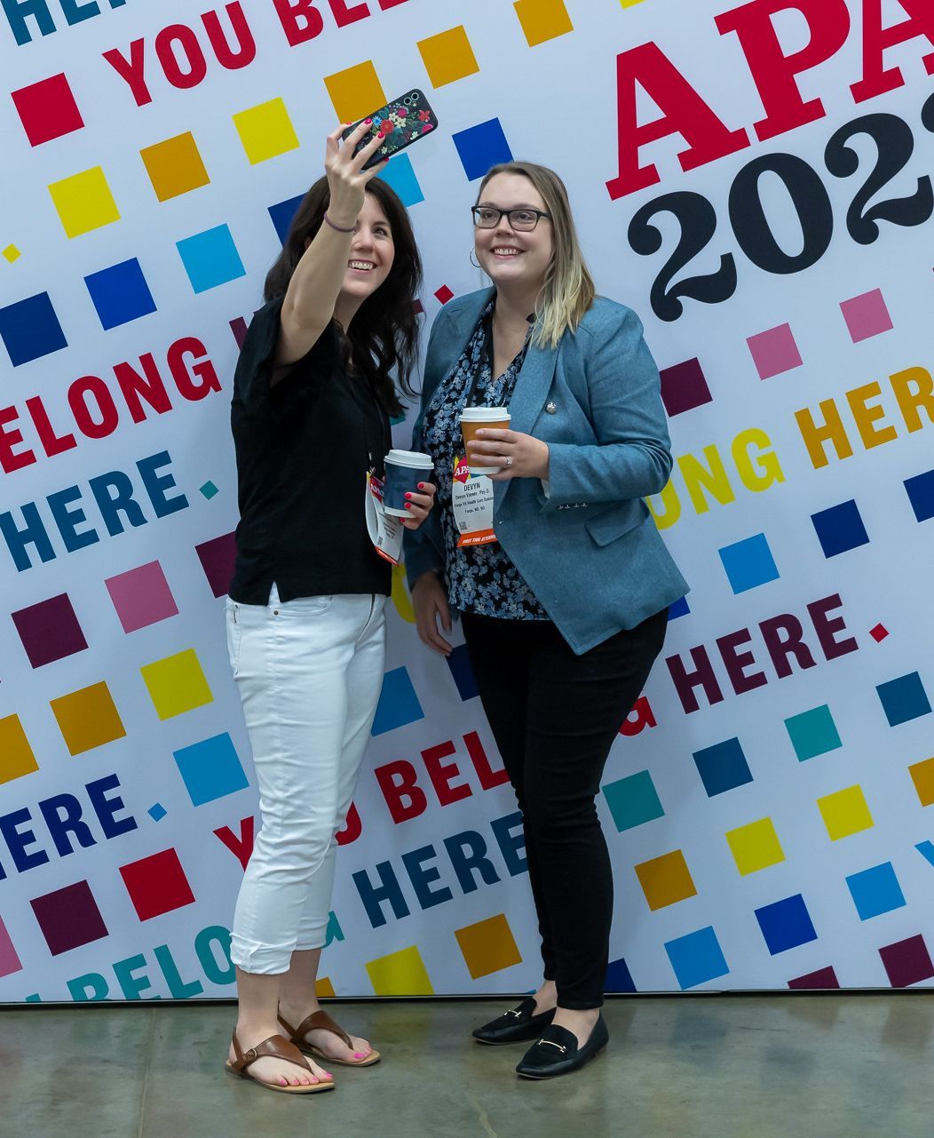 Two attendees take a photo in front of a selfie wall. 