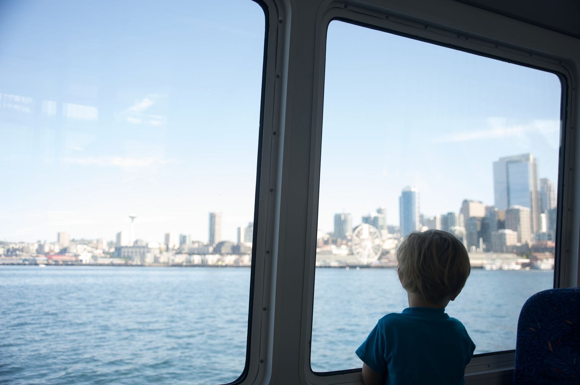 A young boy is looking out of a boat window at the city skyline.