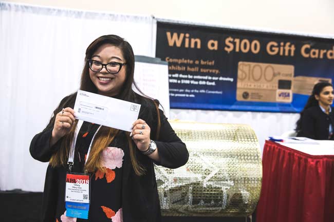 A woman is holding a check in front of a sign that says win a $ 100 gift card.