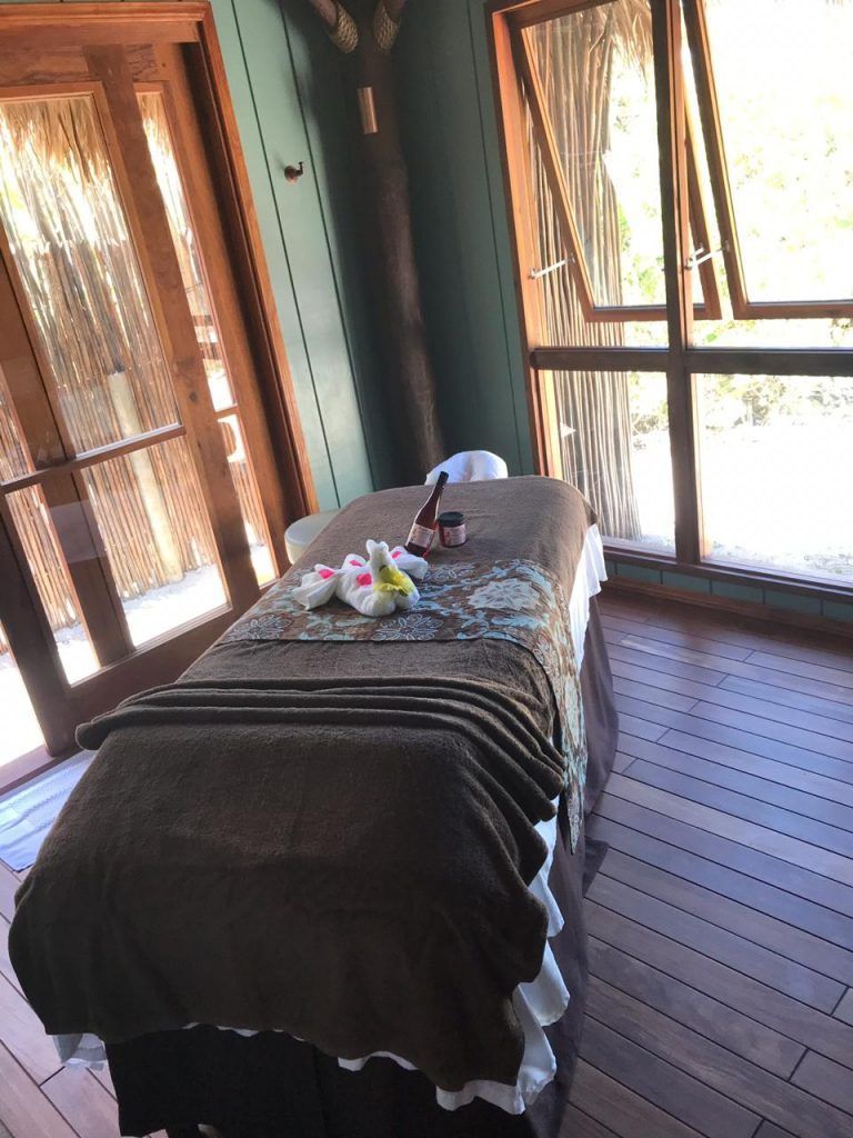Massage table in spa room with wooden floor, open windows, and floral decorations.
