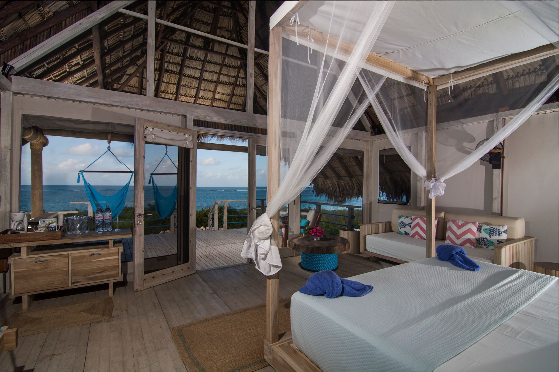 Beachfront bedroom with ocean view, hammock, wooden furniture, white bedding, and mosquito net.